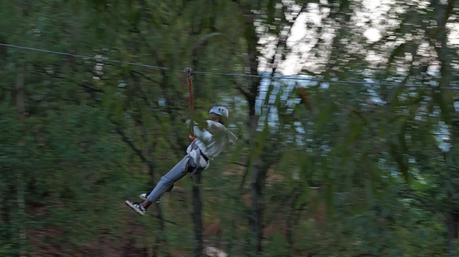 A visitor mid-air on the Fazenda Sengha zip line, harnessed and moving fast through the forest canopy.